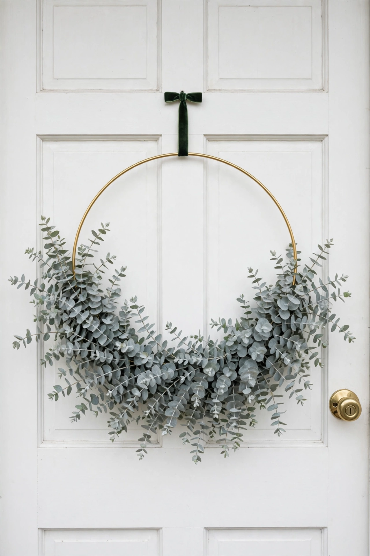 Modern gold hoop wreath with silvery eucalyptus branches on a white front door.